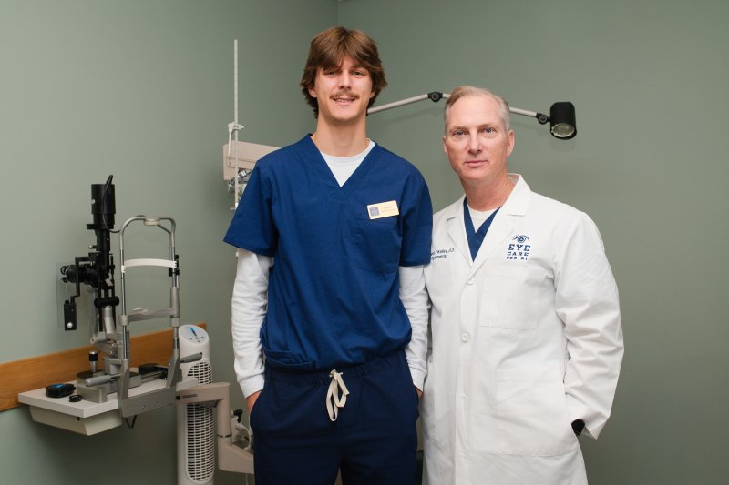Optometrist and intern standing in eye exam room posing for photo.