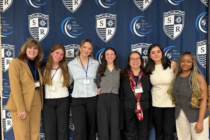 Jessicka and other students smiling in front of a We Mean Business Day backdrop.