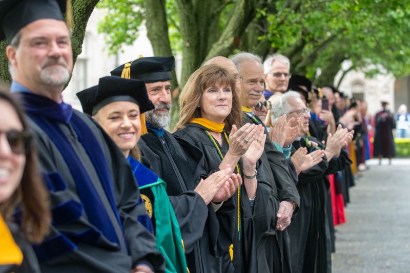 faculty in their regalia clapping as students walk down to graduation.