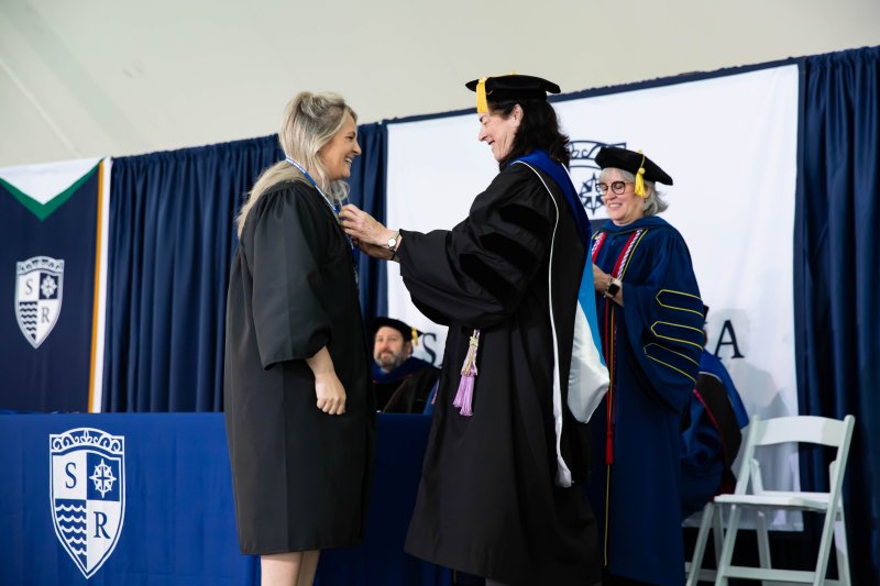 Student and faculty in black robes at nursing pinning ceremony
