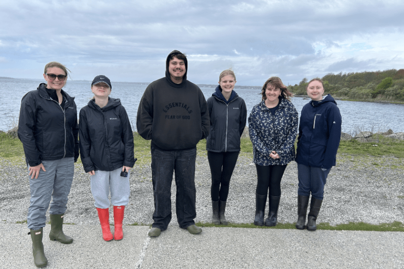 group photo of six people outside in front of the ocean.