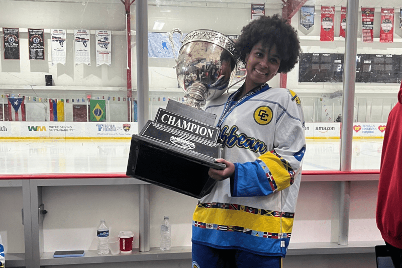 Aryana in hockey jersey holding large trophy.