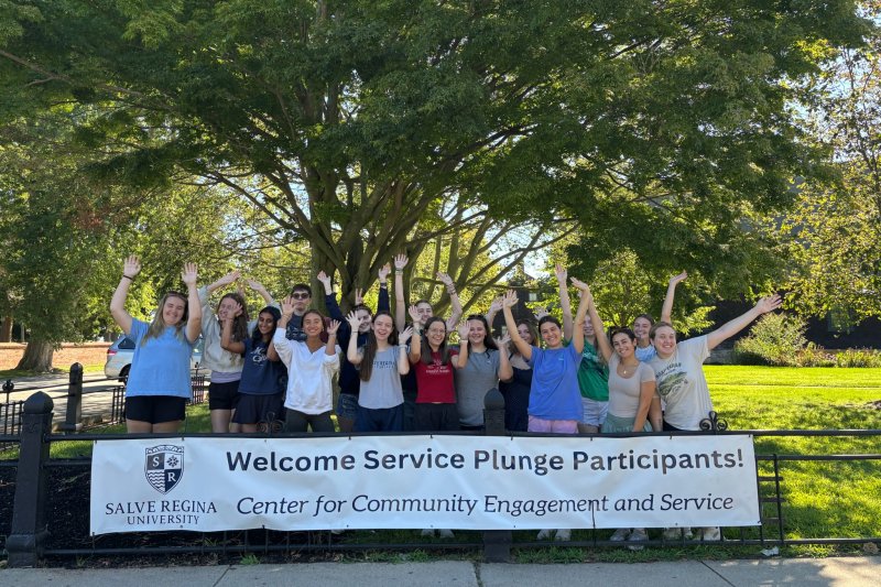 Service Plunge participants pose behind a Salve welcome banner with their hands raised.