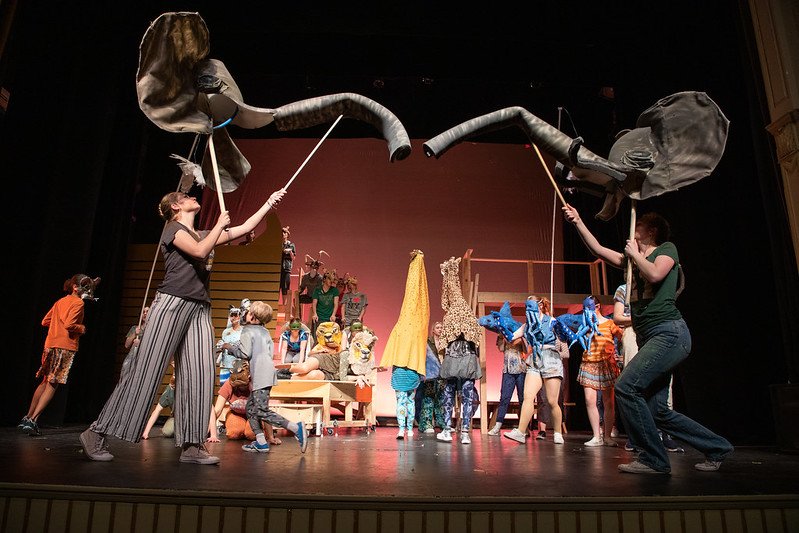 Actors puppetteering large elephant heads on sticks