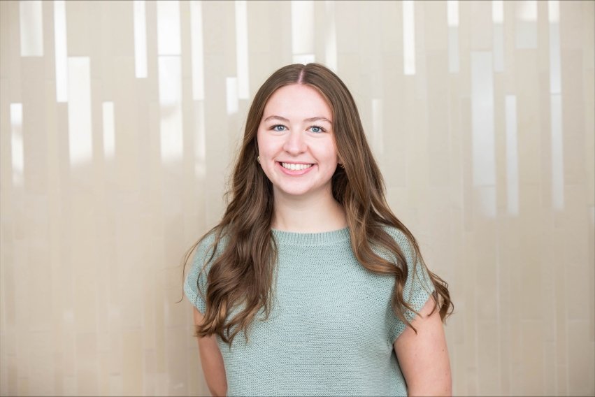 Professional headshot of Spengler in green top in front of beige wall.