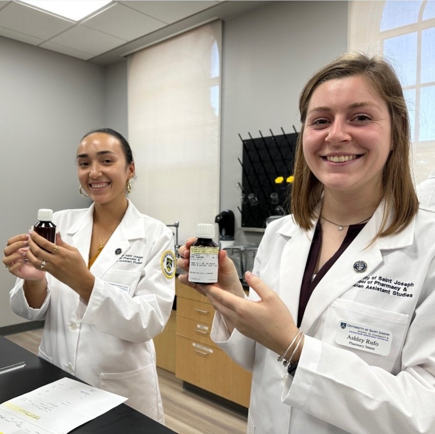 Marro-Wilson smiling with another person wearing their lab coats and holding medicine bottles.