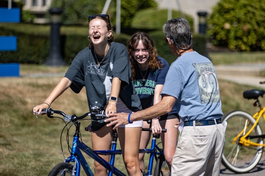 New students laugh and working together to ride a tandem bicycle.