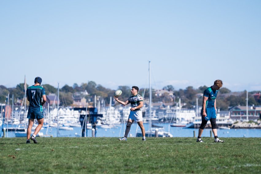 Three men's rugby players on a field that overlooks the water.