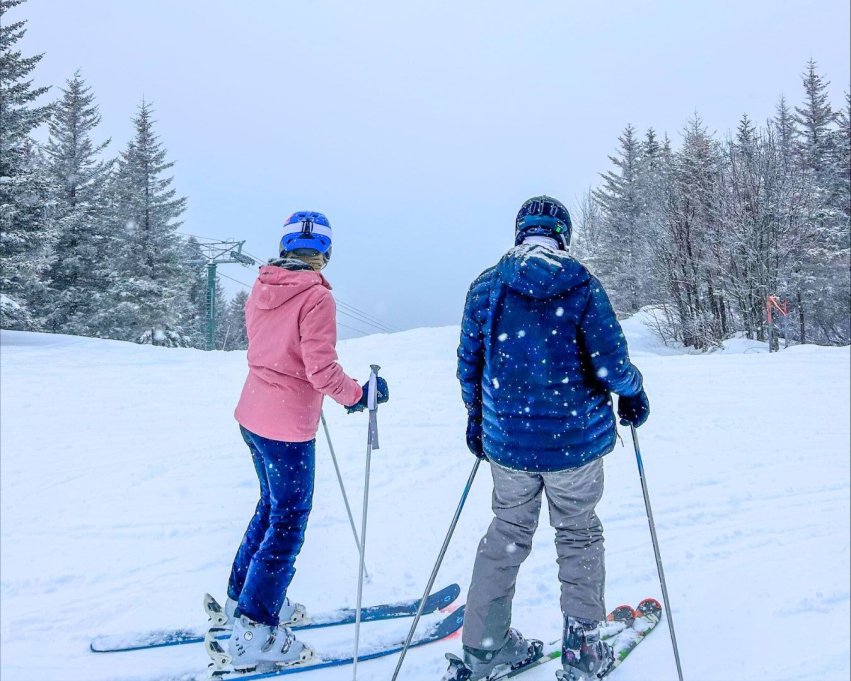 two members of the Ski and Snowboarding Club skiing on the snowy slope in their winter gear.