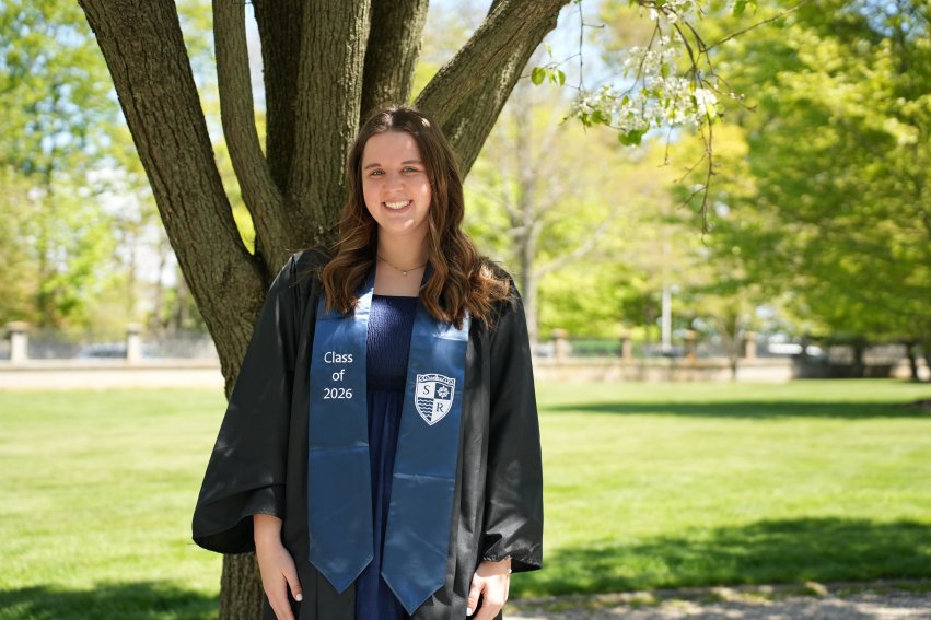Osborne in graduation regalia smiling in front of tree