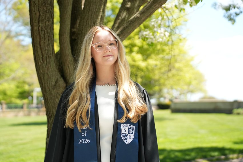 McConaghy in graduation regalia smiling in front of tree