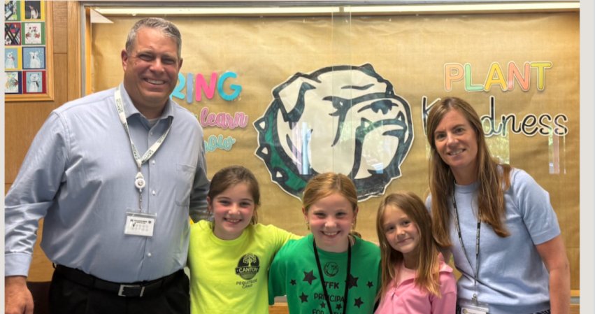 Two educators stand with three smiling students in front of a school display.