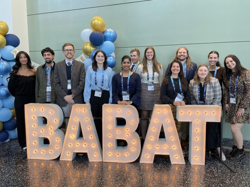 Group of students and professor behind the logo for BABAT