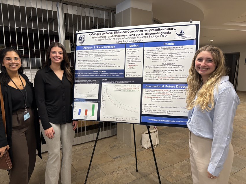 Three women stand beside a research poster on altruism and social distance.