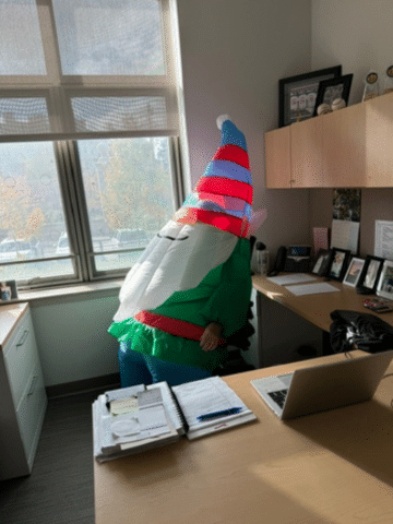Person in garden gnome costume sitting in office chair.