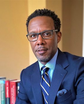Professional headshot of Wilson in navy blue suit and striped tie.