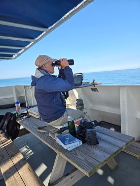 Dr. Jim Chace on a boat looking at the sean through binoculars.