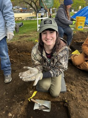 Student at an archaeological excavation site holds a small artifact that was uncovered while working in an excavation unit at Weirs Beach in New Hampshire.