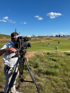NBC Sports camera operator films golfers during a tournament round from the edge of the fairway.