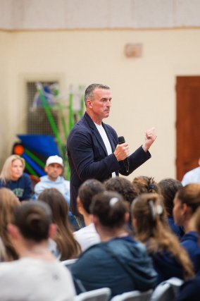 Pro athlete wearing a suit talking to crowd of students seated.