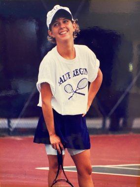 Female tennis player on court standing casually with racquet.