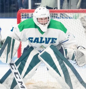 Hockey goalie in pads and helmet guarding the net.