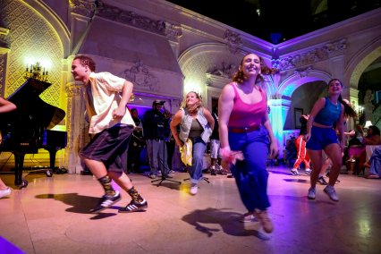 Jazz dancers perform under colored lights in a lounge setting in a great hall.