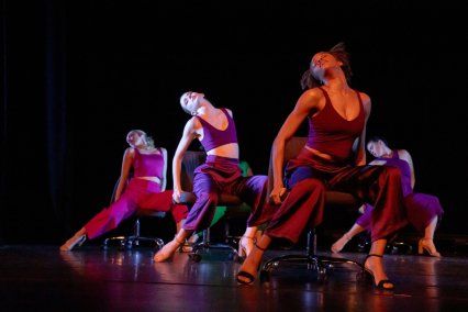 Four dancers positioned dramatically on chairs on a dark stage